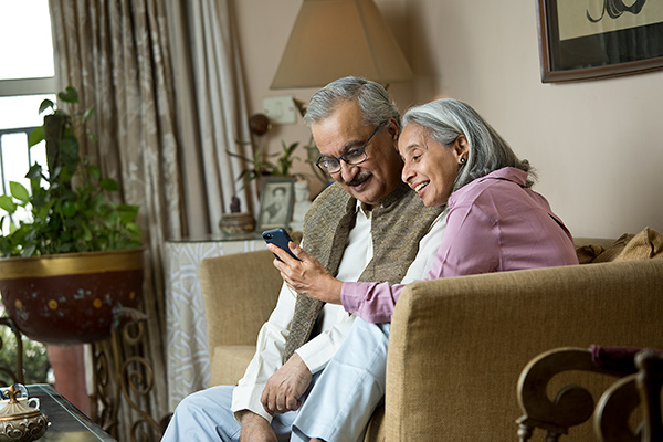 Elder couple sitting on couch looking at smartphone
